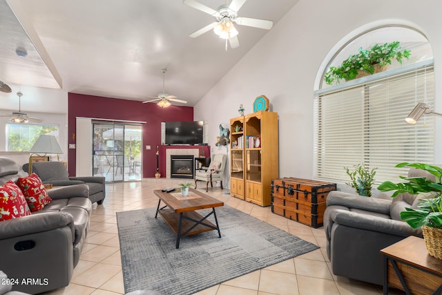 living room with ceiling fan, light tile patterned floors, a tile fireplace, and high vaulted ceiling