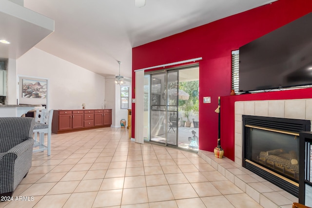 living room featuring ceiling fan, vaulted ceiling, a tile fireplace, and light tile patterned flooring