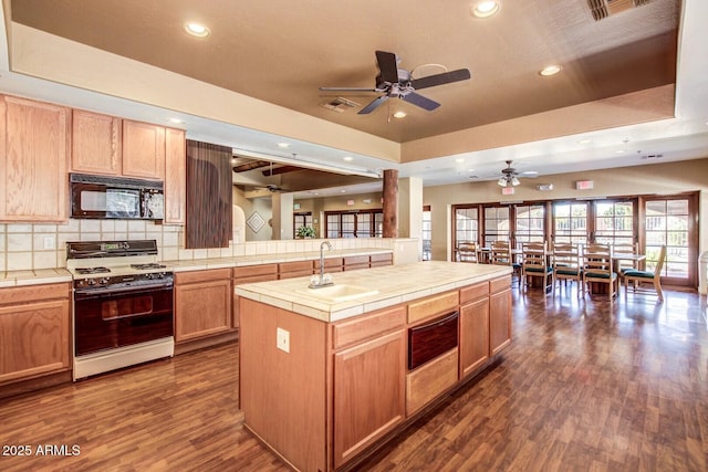 kitchen featuring a tray ceiling, white range with gas stovetop, tile countertops, and a center island