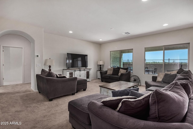 living room featuring arched walkways, recessed lighting, visible vents, and light colored carpet