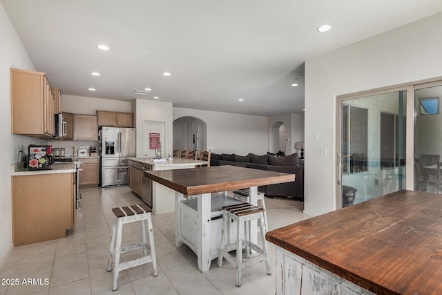 kitchen with arched walkways, a center island with sink, stainless steel appliances, recessed lighting, and a sink