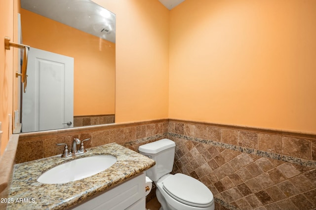 bathroom with a wainscoted wall, toilet, vanity, and tile walls