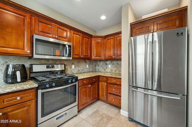 kitchen with light tile patterned floors, light stone counters, backsplash, and appliances with stainless steel finishes