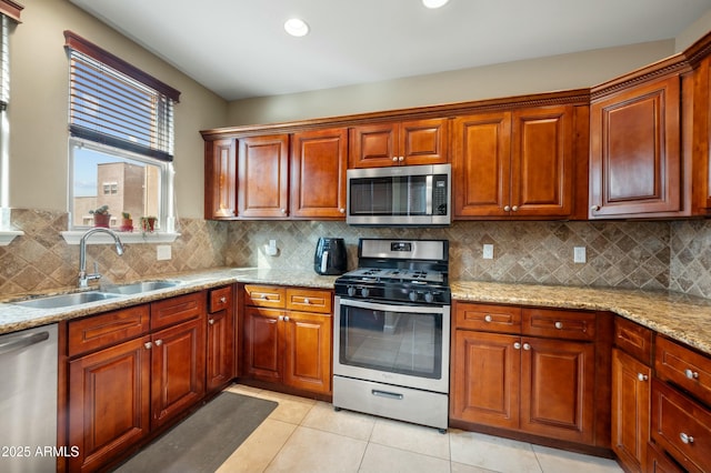 kitchen featuring tasteful backsplash, light stone counters, appliances with stainless steel finishes, light tile patterned flooring, and a sink