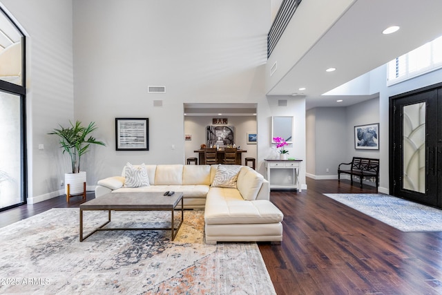 living room with a towering ceiling and dark wood-type flooring