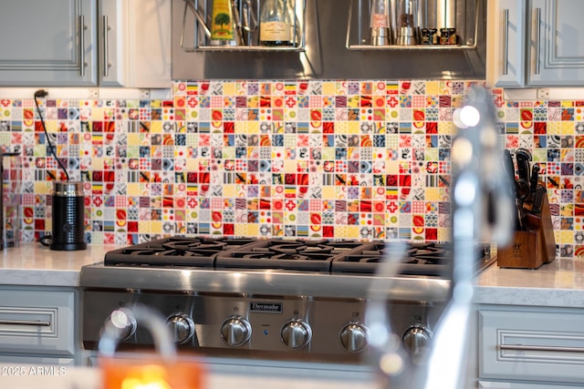 kitchen featuring gray cabinetry, decorative backsplash, light stone countertops, and stainless steel gas stovetop