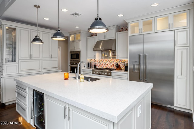 kitchen featuring a center island with sink, sink, built in appliances, and decorative light fixtures