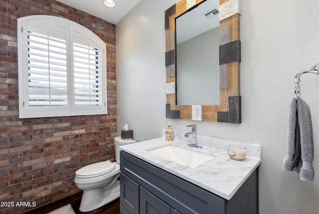 bathroom with vanity, toilet, and brick wall