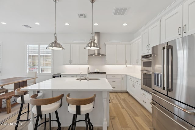 kitchen featuring light countertops, hanging light fixtures, visible vents, appliances with stainless steel finishes, and wall chimney exhaust hood