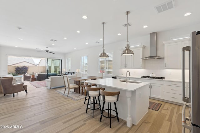 kitchen with visible vents, hanging light fixtures, light countertops, wall chimney range hood, and white cabinetry