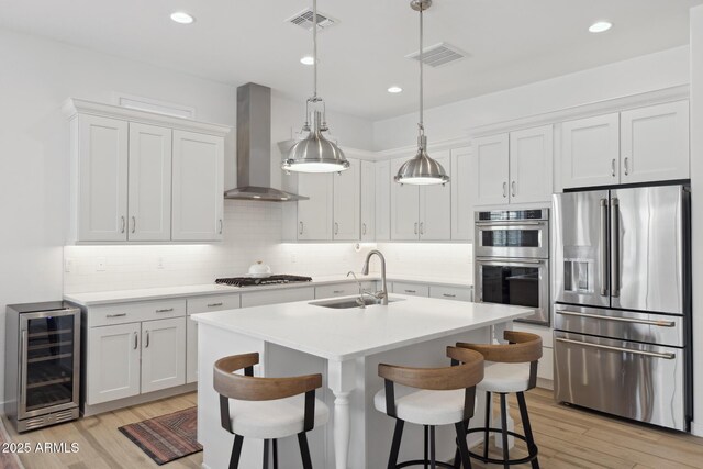 kitchen featuring stainless steel appliances, white cabinetry, a sink, wall chimney range hood, and beverage cooler