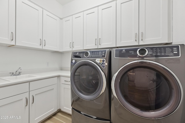 laundry area with washer and clothes dryer, a sink, cabinet space, and light wood-style floors