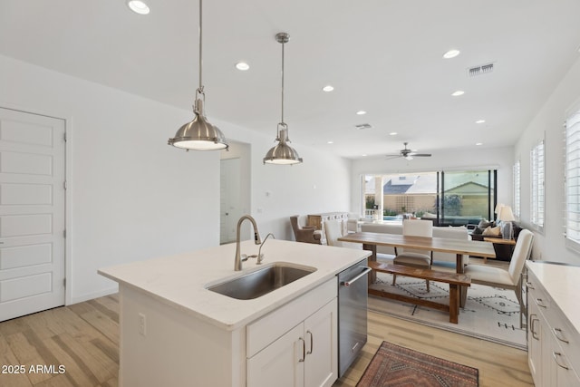 kitchen with white cabinets, open floor plan, decorative light fixtures, a kitchen island with sink, and a sink