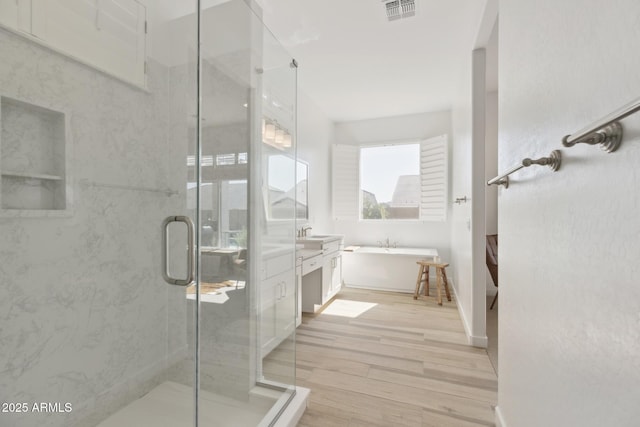 full bathroom featuring a stall shower, visible vents, a soaking tub, wood finished floors, and vanity