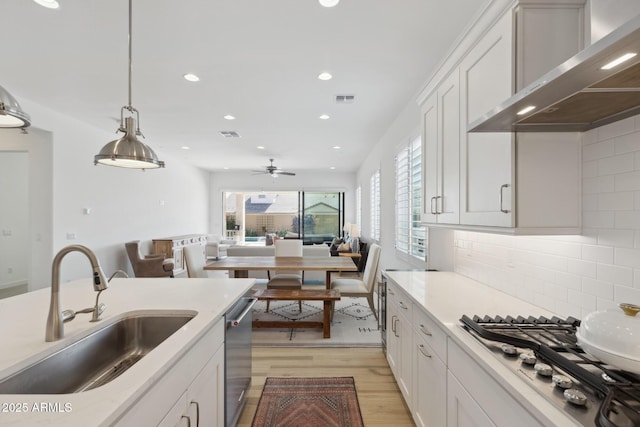 kitchen with wall chimney range hood, white cabinetry, a sink, and decorative light fixtures