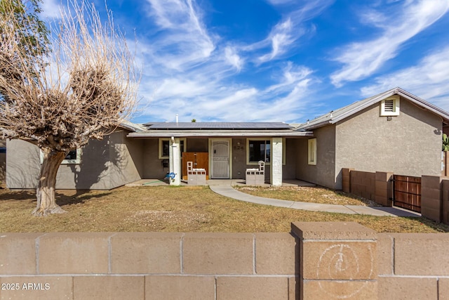 ranch-style home with stucco siding, solar panels, a porch, and fence