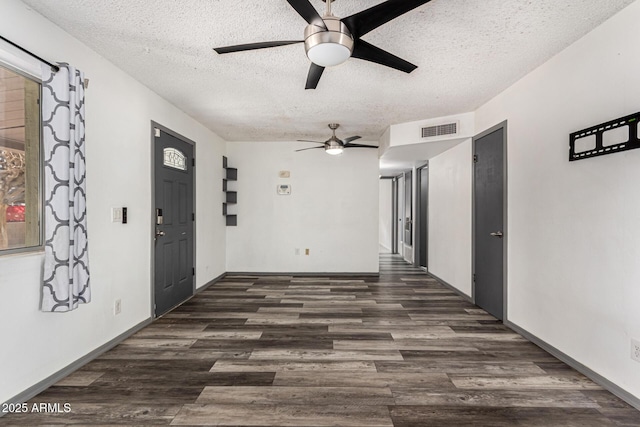 unfurnished room with a textured ceiling, ceiling fan, visible vents, and dark wood-style flooring