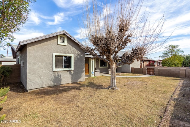 back of property featuring stucco siding, a yard, and fence