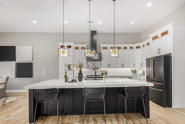 kitchen with a large island, wall chimney range hood, pendant lighting, high end fridge, and light wood-type flooring