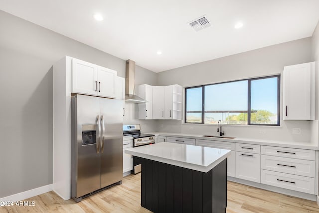 kitchen with wall chimney exhaust hood, stainless steel appliances, a center island, light hardwood / wood-style floors, and white cabinetry