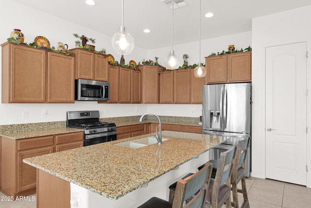 kitchen featuring a breakfast bar, sink, decorative light fixtures, stainless steel appliances, and a kitchen island with sink