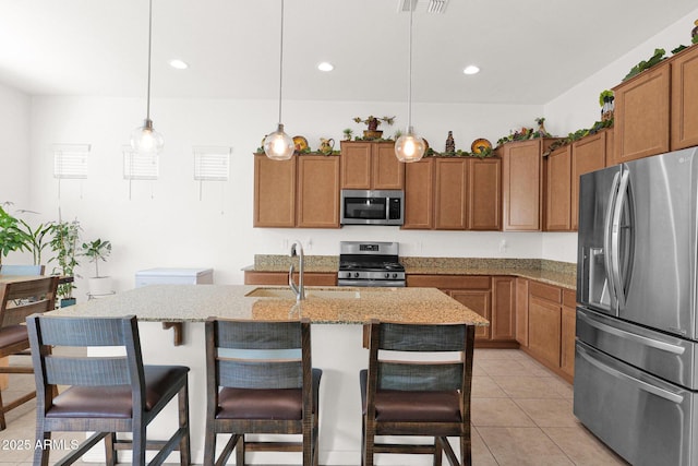 kitchen with stainless steel appliances, an island with sink, pendant lighting, and light tile patterned flooring