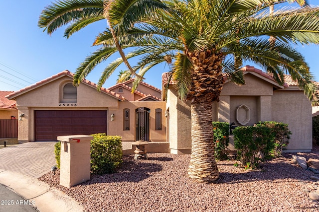 mediterranean / spanish-style house featuring stucco siding, a garage, a tiled roof, and decorative driveway