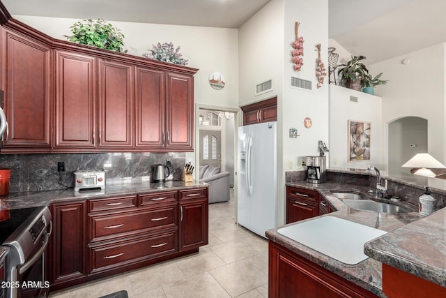 kitchen featuring white fridge with ice dispenser, high vaulted ceiling, stainless steel range oven, and sink