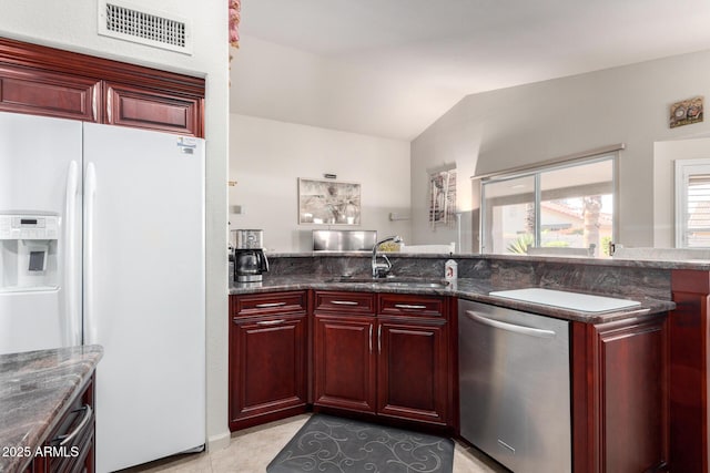 kitchen featuring dishwasher, white fridge with ice dispenser, sink, dark stone countertops, and vaulted ceiling