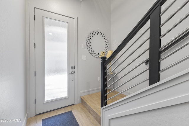 entryway featuring baseboards, light wood finished floors, and stairs