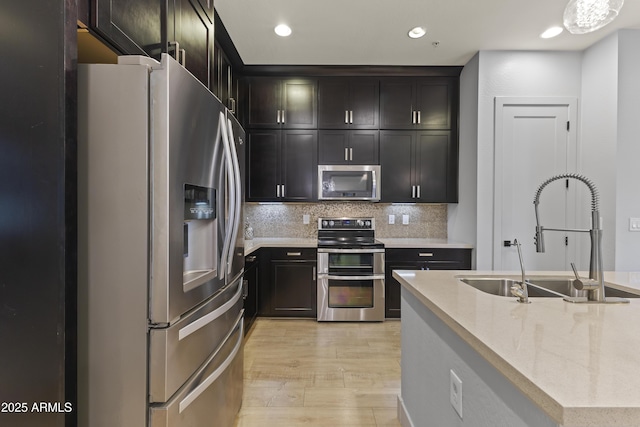 kitchen with tasteful backsplash, light wood-style flooring, light stone counters, appliances with stainless steel finishes, and a sink