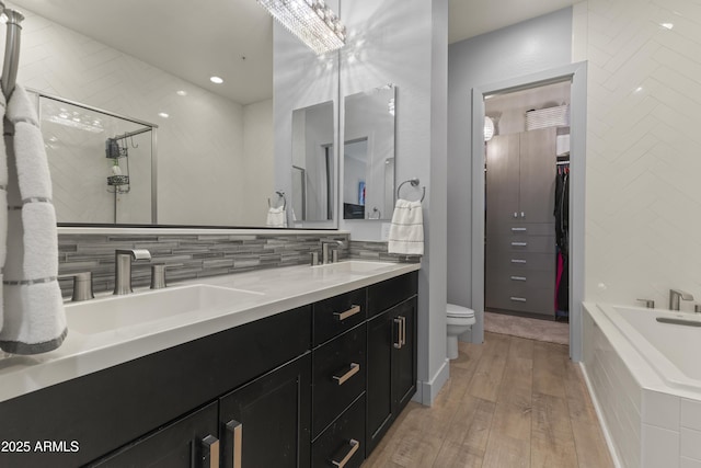 bathroom featuring decorative backsplash, a sink, double vanity, a bath, and wood finished floors