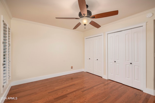 unfurnished bedroom with hardwood / wood-style floors, two closets, ceiling fan, and crown molding