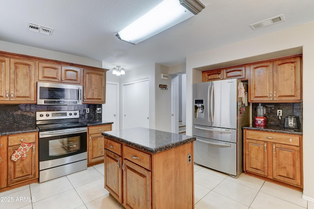 kitchen with stainless steel appliances, visible vents, light tile patterned flooring, and dark stone counters