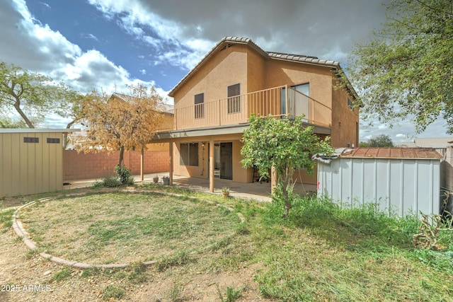 rear view of house with stucco siding, a patio, fence, a storage shed, and an outdoor structure