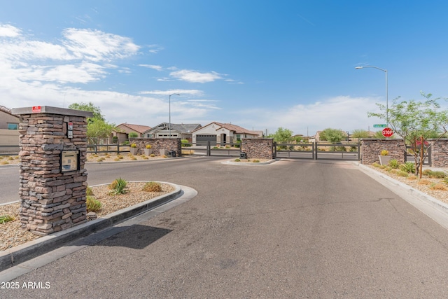 5957 N 89th Dr, Glendale, AZ 85305 - view of asphalt street featuring a gate, street lighting, curbs, a gated entry, and traffic signs