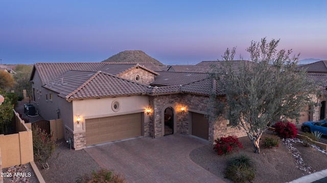 view of front facade featuring a tile roof, stone siding, stucco siding, decorative driveway, and a garage