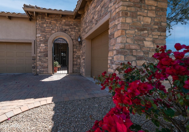 doorway to property with stone siding, an attached garage, stucco siding, and decorative driveway