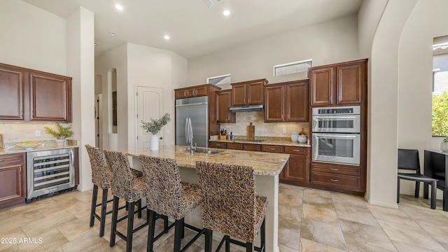 kitchen with light stone countertops, stainless steel appliances, wine cooler, arched walkways, and a sink