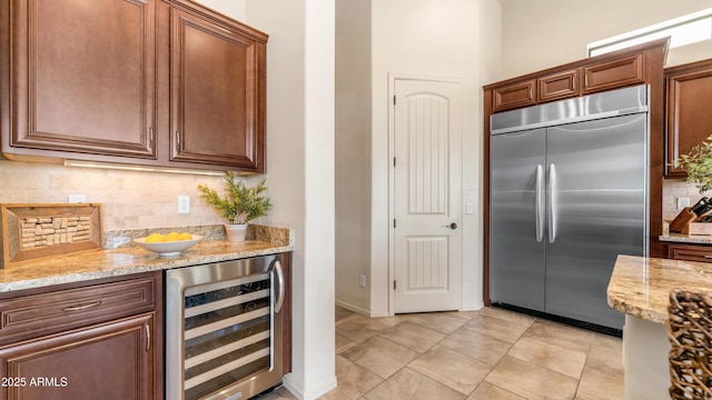 kitchen with decorative backsplash, light stone countertops, wine cooler, stainless steel built in fridge, and light tile patterned floors