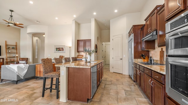 kitchen with appliances with stainless steel finishes, arched walkways, a sink, open floor plan, and a kitchen breakfast bar