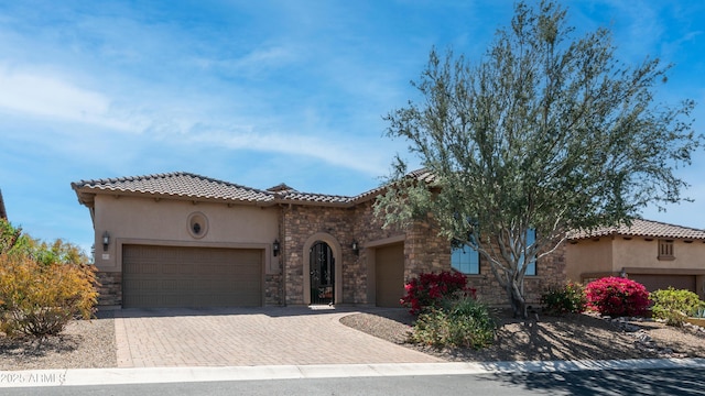 mediterranean / spanish home featuring driveway, a tile roof, stone siding, stucco siding, and a garage