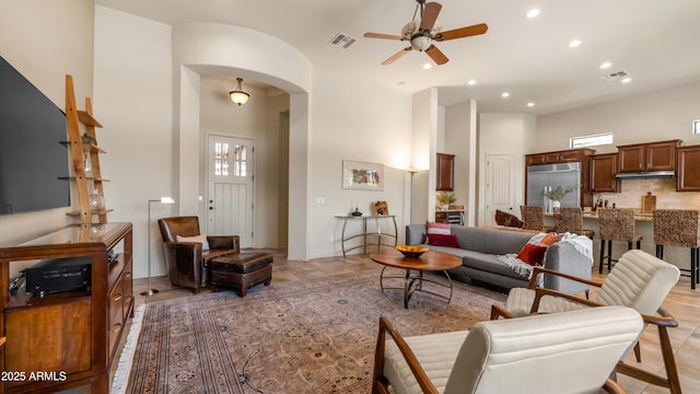 living area with visible vents, a high ceiling, arched walkways, and ceiling fan