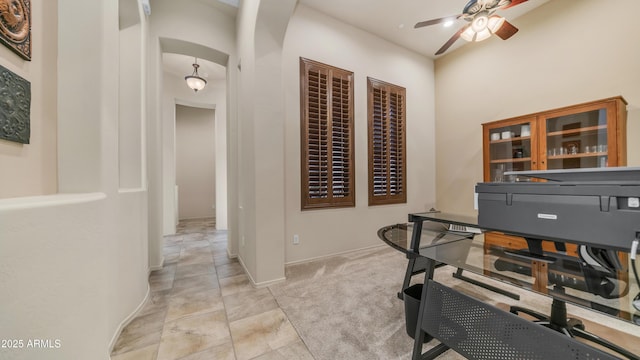 office area with arched walkways, a ceiling fan, light carpet, and baseboards