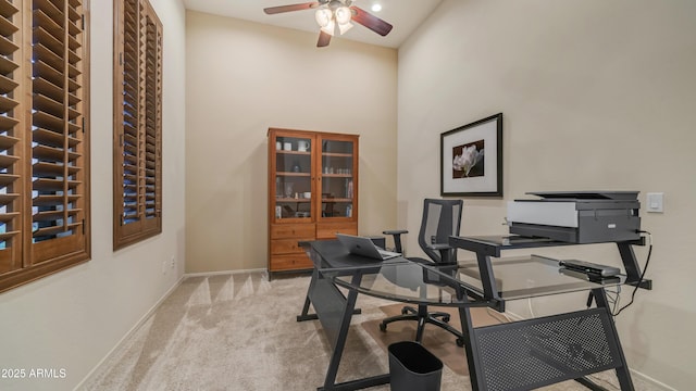 office area featuring baseboards, a towering ceiling, a ceiling fan, and light carpet