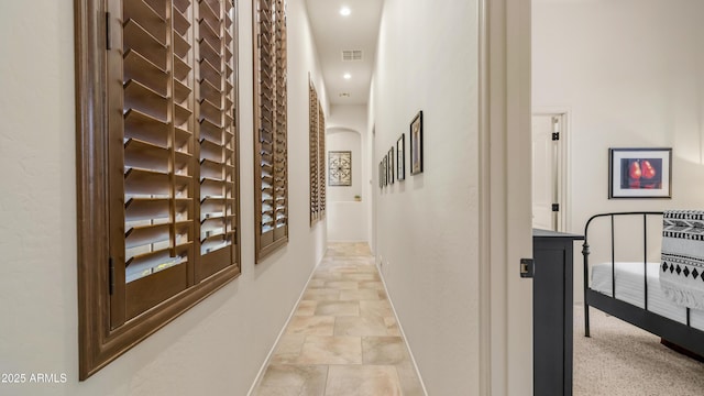 hallway featuring visible vents, stone finish flooring, baseboards, recessed lighting, and arched walkways