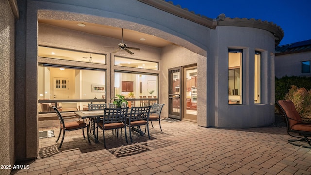 patio at night with outdoor dining area and ceiling fan