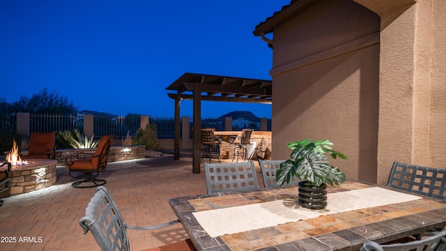 patio at twilight featuring a fire pit, a pergola, fence, and outdoor dining space