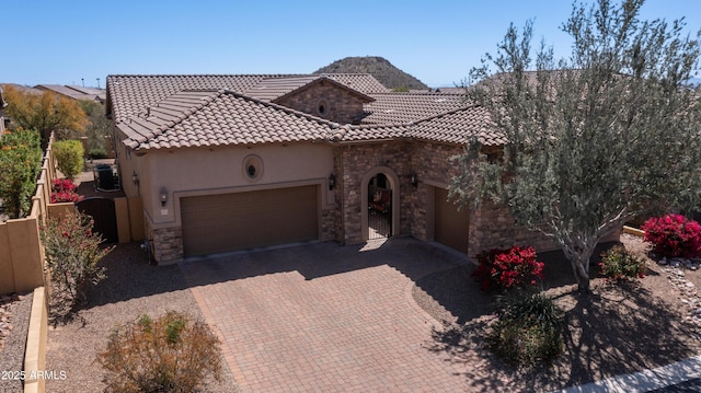 mediterranean / spanish-style home featuring stone siding, stucco siding, an attached garage, a tiled roof, and decorative driveway