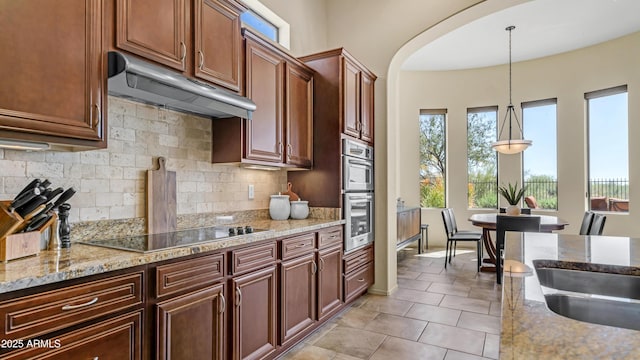 kitchen with black electric cooktop, arched walkways, under cabinet range hood, decorative light fixtures, and backsplash